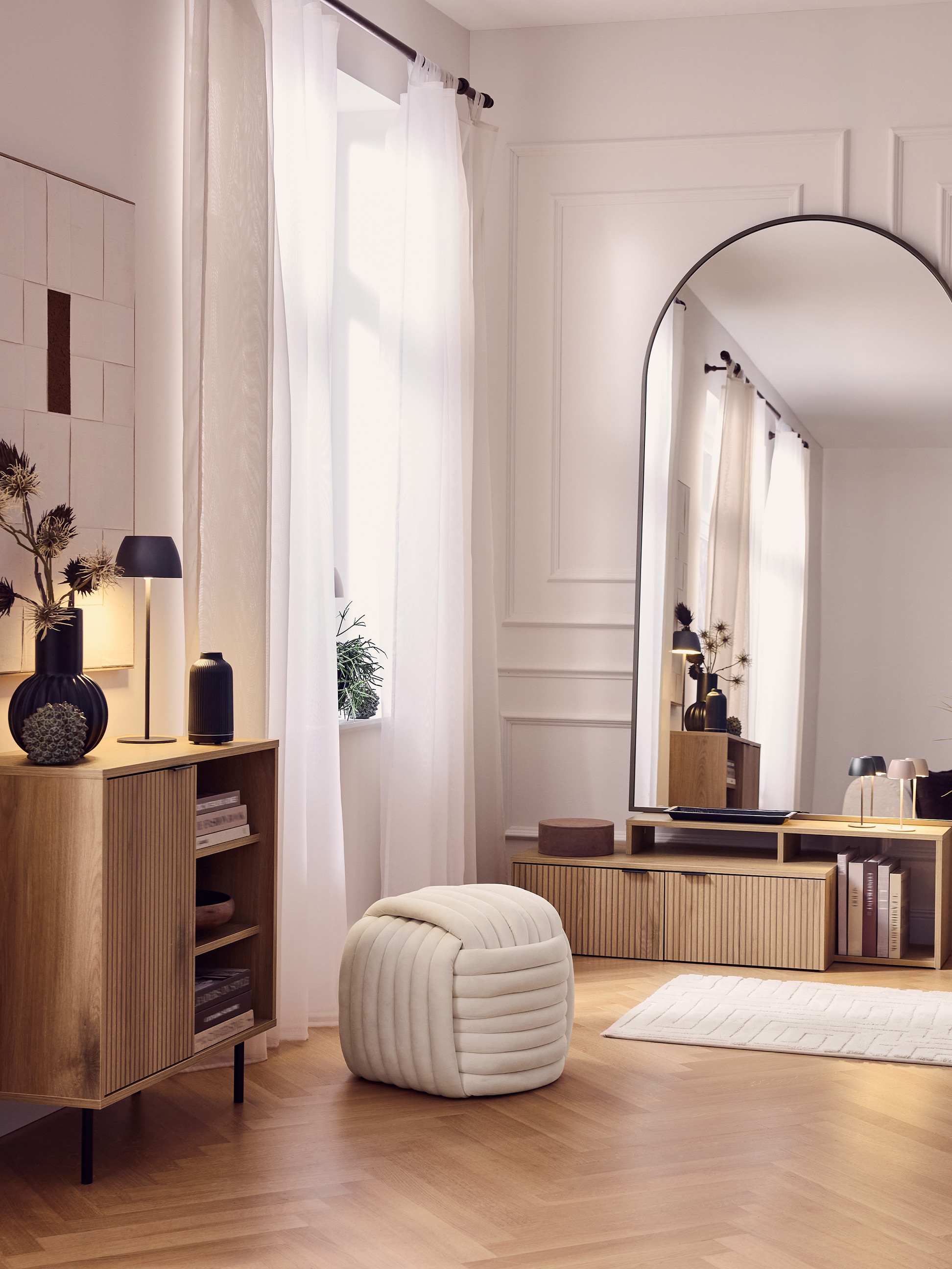 Modernes Wohnzimmer mit Holzschränken, großem Spiegel, Pouf und weißen Vorhängen.