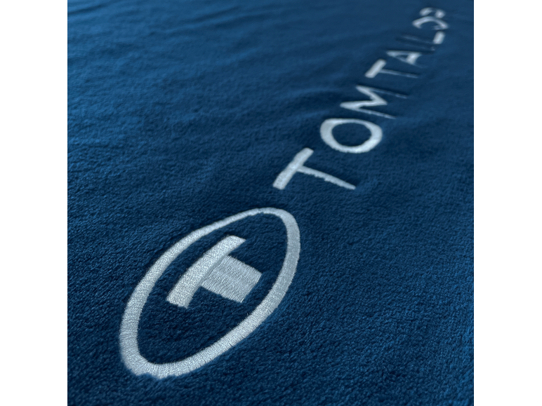 Dunkelblauer Stoff mit einem weißen gestickten Logo und dem Wort „TOM TAILOR“.