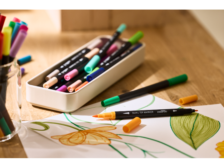 Bunte Dual-Tip-Marker und Zeichnungen auf einem Holztisch.