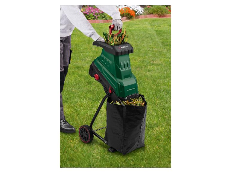 Person im Garten benutzt einen grünen Gartenhäcksler mit schwarzem Auffangsack.