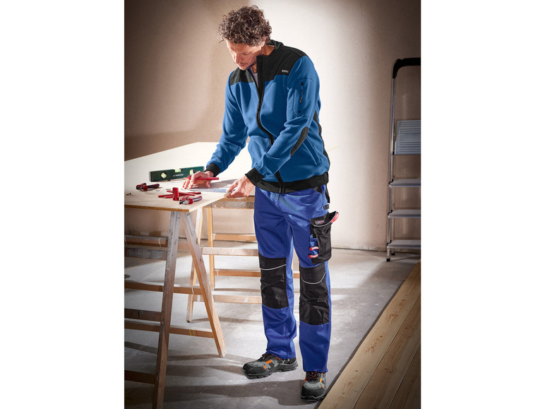 Mann in blauer Arbeitskleidung mit schwarzen Details und Werkzeugtaschen