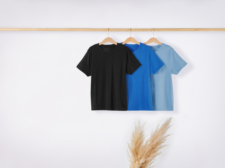 Drei T-Shirts, schwarz, dunkelblau und hellblau, hängen an einem Holzbügel.