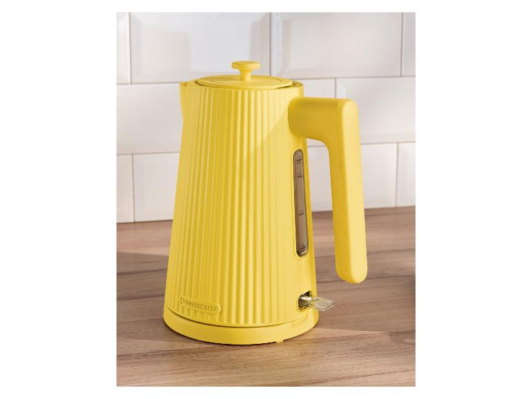 Gelber gerippter SilverCrest Wasserkocher auf einer Holztheke mit weißem Fliesenspiegel.