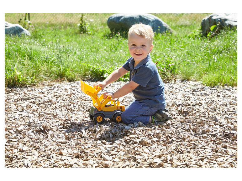 Ein kleiner Junge spielt mit einem gelben Spielzeugbagger auf einem Spielplatz.
