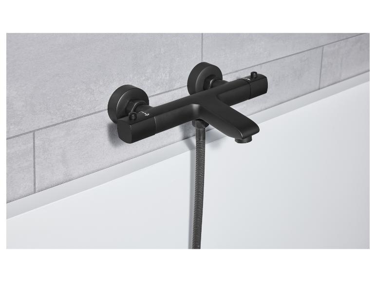 Eine schwarze, matte Badewannenarmatur mit Duschkopf ist an einer grauen, gefliesten Wand montiert.