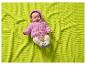 Baby in rosa Kapuzenpullover und beiger Hose auf einer lindgrünen Waffeldecke.