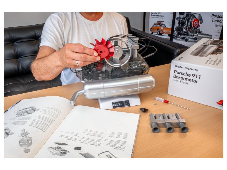 Eine Person baut ein Porsche 911 Boxermotor-Modell von Franzis zusammen, mit Anleitung und Verpackung auf einem Tisch.