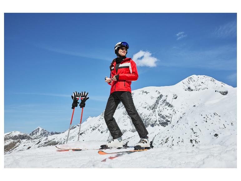 Skifahrerin in roter Jacke, schwarzer Hose, Helm und Skibrille am Berg.