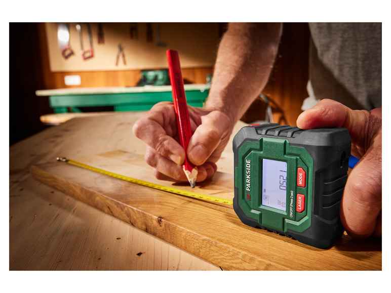 Eine Person misst mit einem Parkside Laser-Maßband auf einer Holzplatte.
