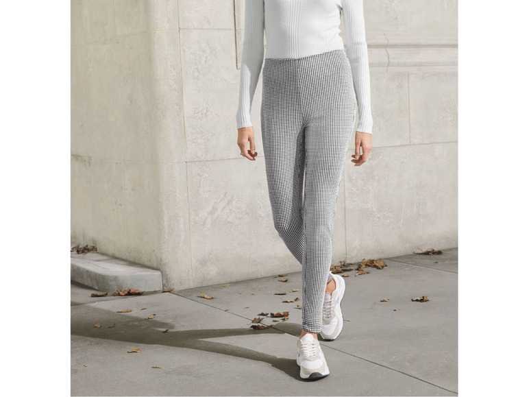 Frau mit weißem Pullover und schwarzen Hosen mit weißen Sneakern.