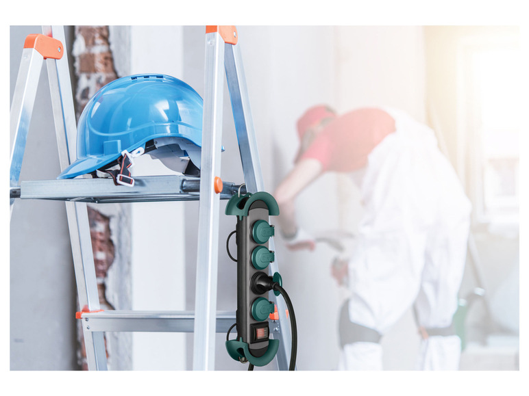 Ein blauer Helm und eine Steckdosenleiste hängen an einer Leiter.