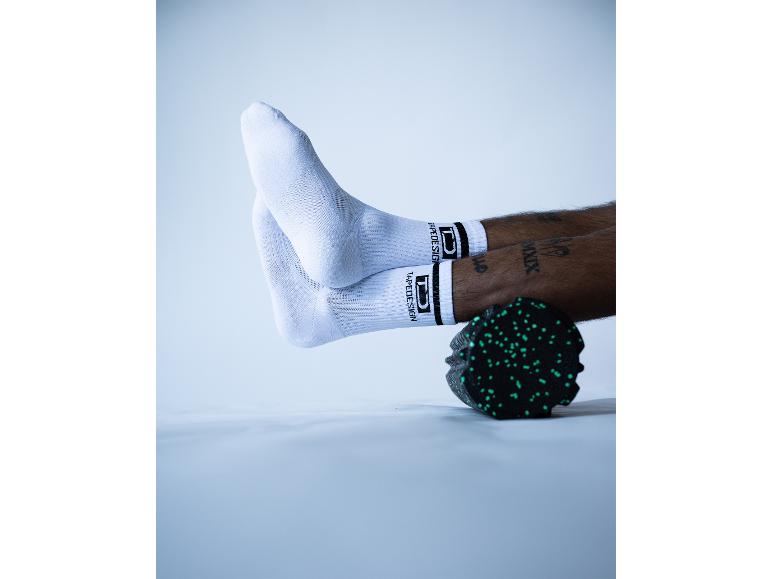 Füße in weißen Tapedesign-Socken auf einer schwarzen Faszienrolle.
