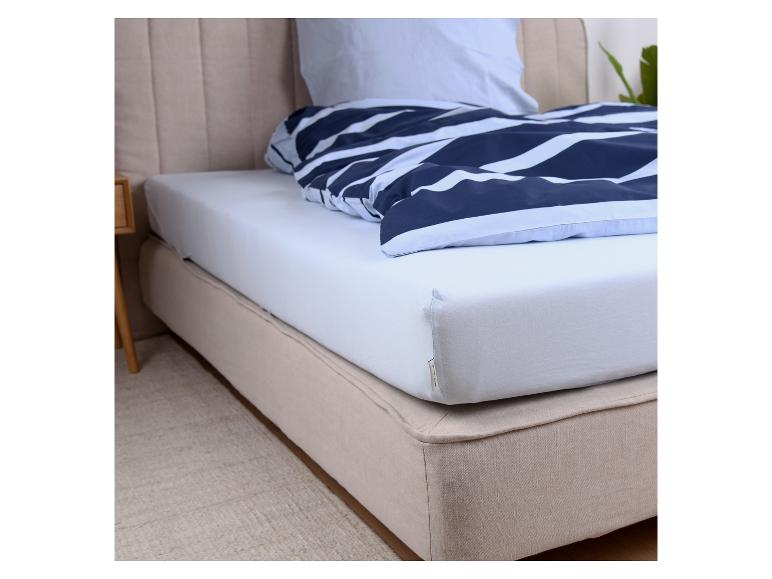 Bett mit weißem Spannbettlaken und blau gestreifter Bettdecke.