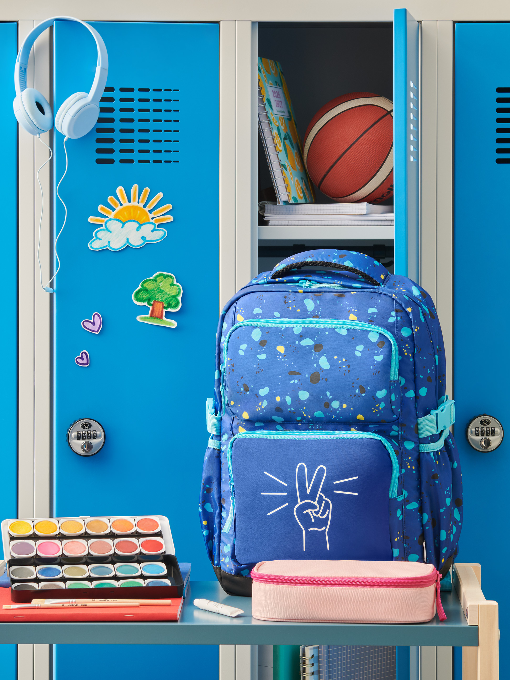 Blauer Rucksack mit Friedenszeichen, Kopfhörer, Aquarellfarben und Schulmaterial in einem Spind.