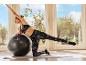 Eine Frau in Sportkleidung trainiert auf einer Matte mit einem Gymnastikball.