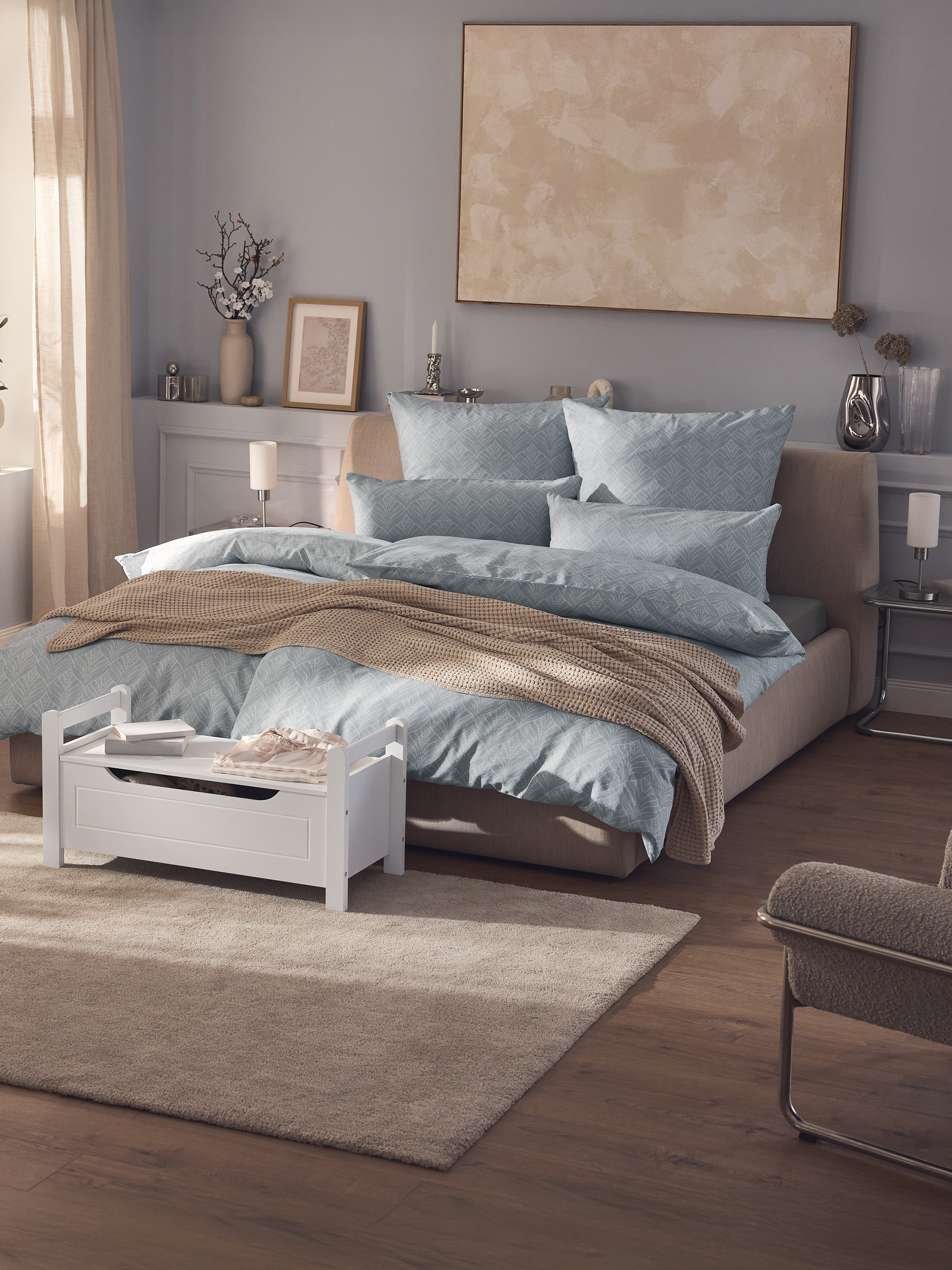 Modernes Schlafzimmer mit Doppelbett, blauer gemusterter Bettwäsche, beigem Überwurf und weißer Aufbewahrungsbank.