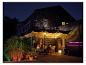 Menschen genießen Abendessen auf einer Terrasse mit farbiger LED-Beleuchtung und Grill.