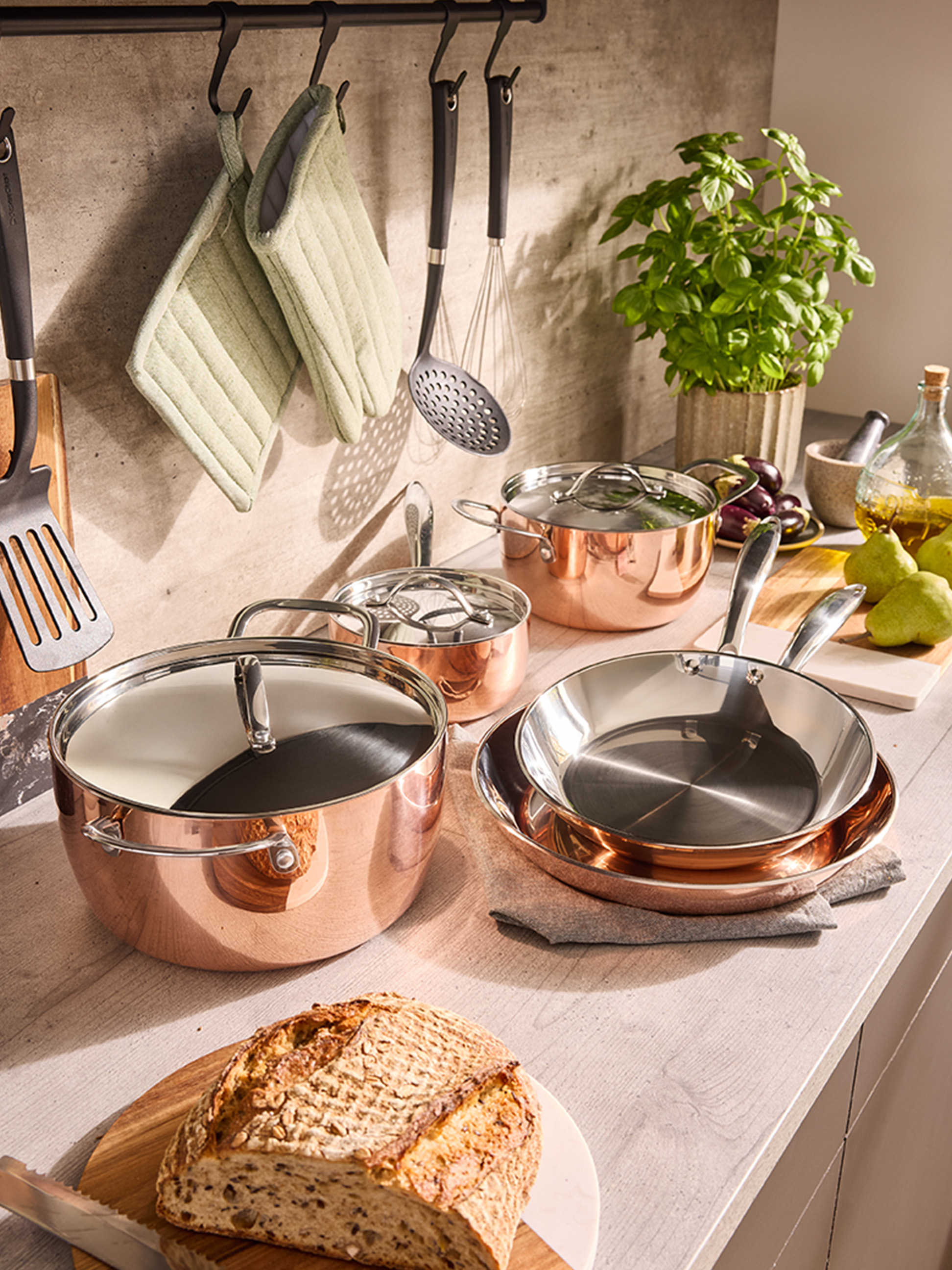 Set aus Kupferkochgeschirr und Pfannen auf einer Küchenarbeitsplatte, mit Brot und Kräutern.