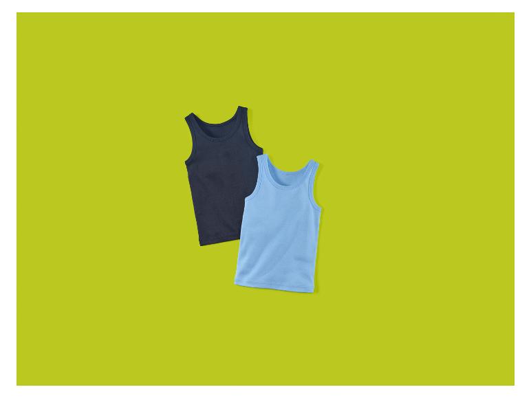 Zwei Kinder-Unterhemden, ein dunkelblaues und ein hellblaues, auf grünem Hintergrund.