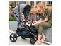 Mutter lächelt Baby im grauen Kinderwagen, grüner Overall, städtische Umgebung.