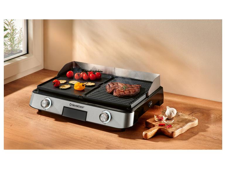 Elektrischer Grill mit Fleisch und Gemüse, dazu Knoblauch und Chilis.