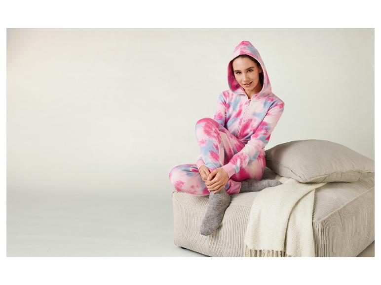 Eine Frau in einem rosa-blauen Tie-Dye-Onesie sitzt auf einer Couch.