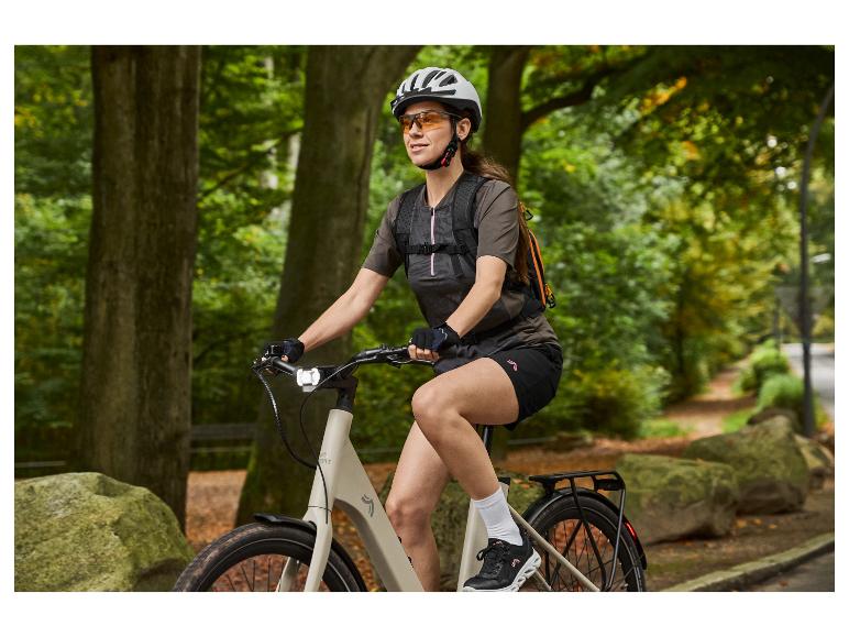 Frau auf Crivit E-Bike mit Helm und Rucksack, auf einem Waldweg.