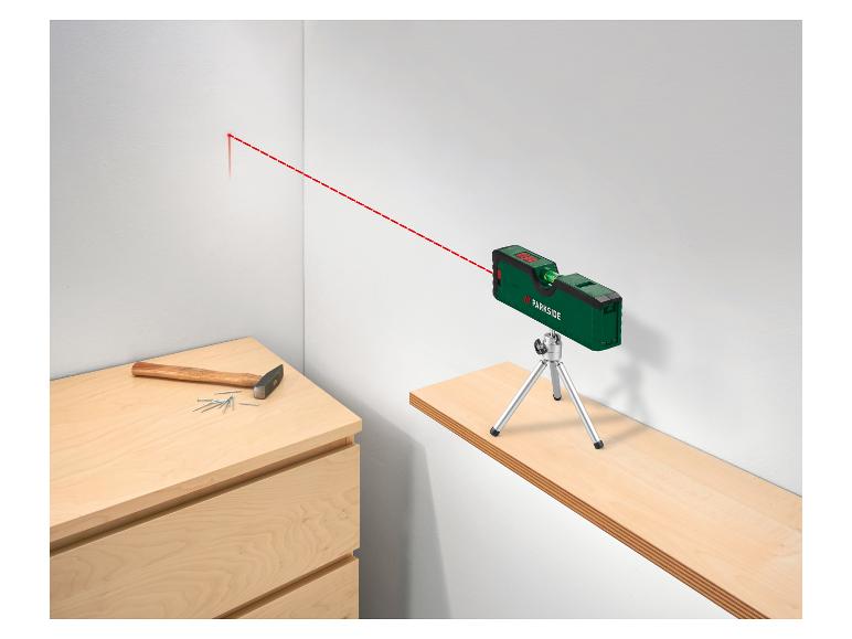 Grüner Laserwasserwaage mit Stativ projiziert rote Linie an Wand, mit Hammer und Nägeln.