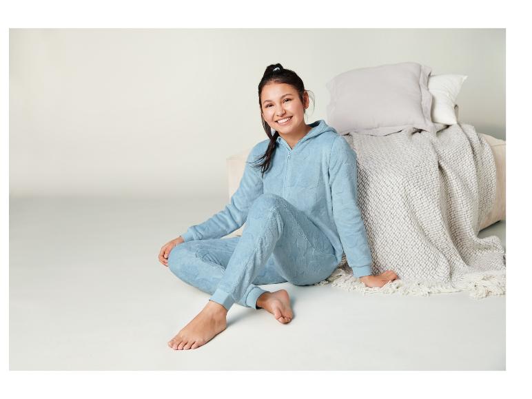 Eine Frau in einem blauen Pyjama mit Sternenmuster sitzt auf dem Boden mit einer weißen Decke hinter sich.