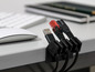 Ein schwarzer Kabelclip mit USB- und Ethernet-Kabeln auf einem Schreibtisch.