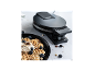 Waffeln mit Blaubeeren und Nüssen auf einem schwarzen Teller, Waffeleisen im Hintergrund.