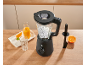 Schwarzer Mixer mit Eis, Orangensaft und einer Orangenscheibe auf einem Holztisch.