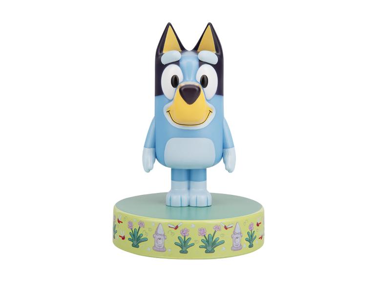 Blaue Cartoon-Hundefigur auf grünem Sockel mit Gartenmotiv.