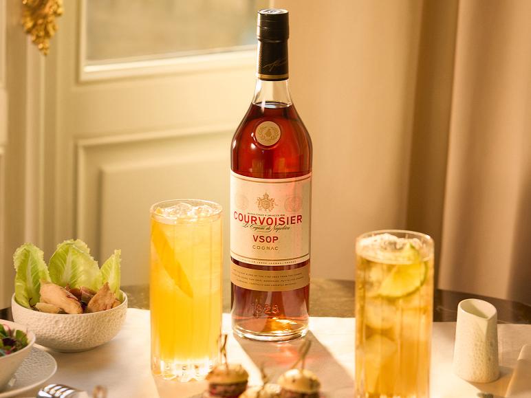 Cognacflasche mit zwei Drinks und Snacks auf einem Tisch.