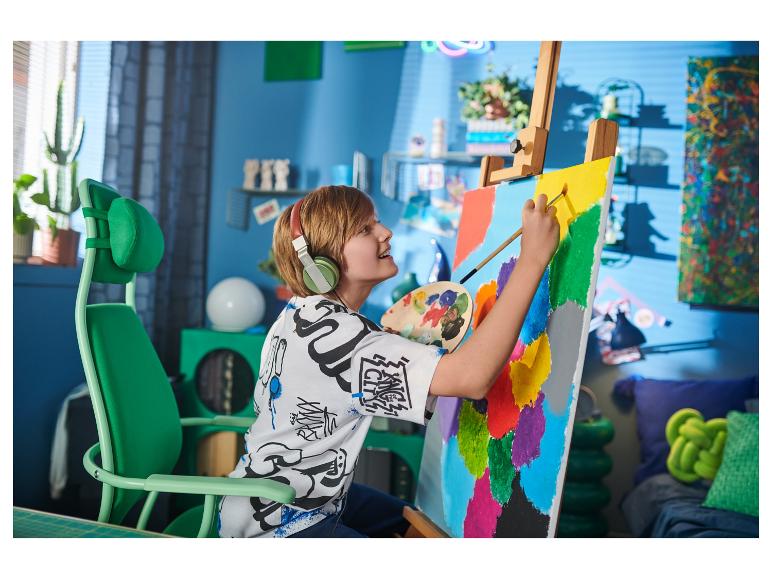 Blonder Junge mit Kopfhörern malt auf Leinwand in einem grünen Stuhl.
