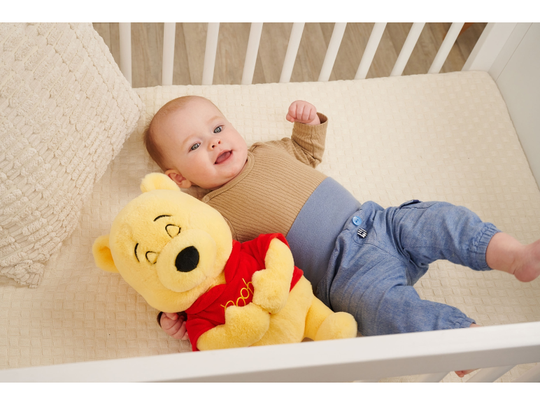 Lächelndes Baby liegt im Kinderbett mit einem Teddybär.