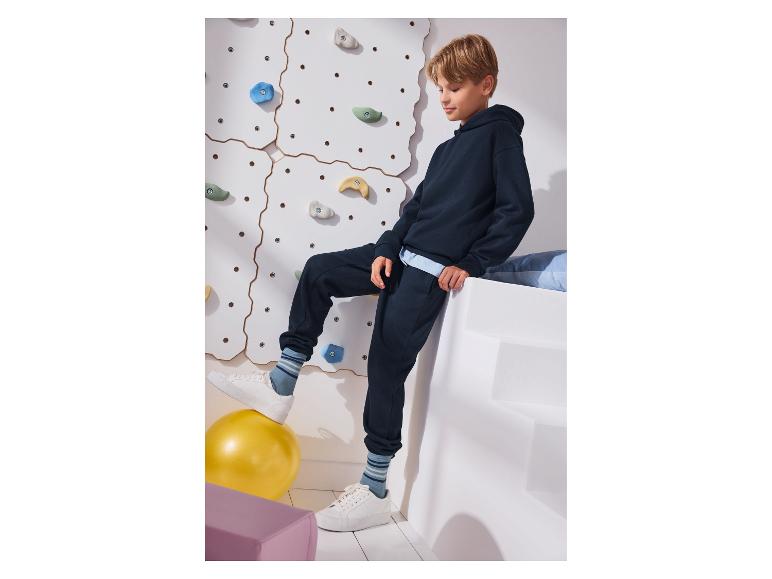 Junge in marineblauem Hoodie und Jogginghose, mit einem Fuß auf einem gelben Ball.