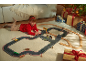 Mädchen spielt mit Autorennbahn und Holzeisenbahn, Weihnachtsgeschenke im Hintergrund.
