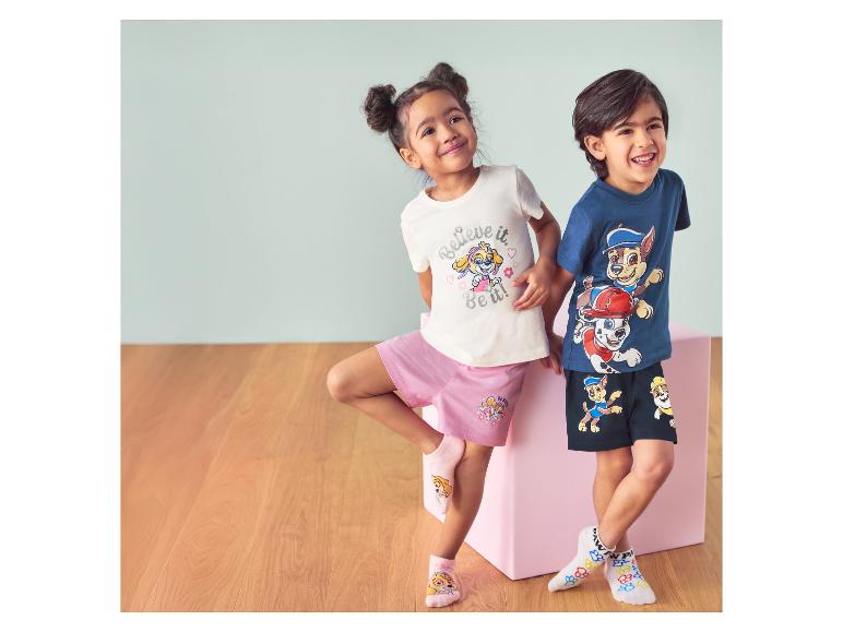 Zwei Kinder in Paw Patrol-Socken und -Kleidung, lächelnd vor einer rosa Box.