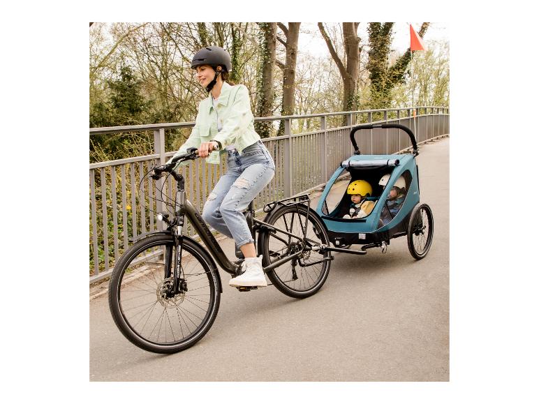 Frau auf E-Bike zieht Fahrradanhänger mit zwei Kindern.