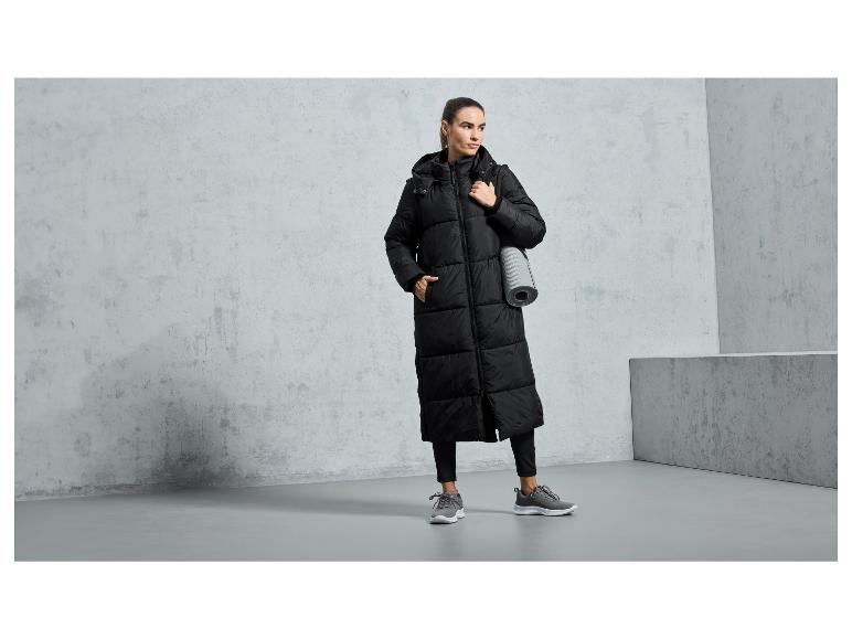 Eine Frau trägt einen langen, schwarzen Wintermantel und graue Turnschuhe.