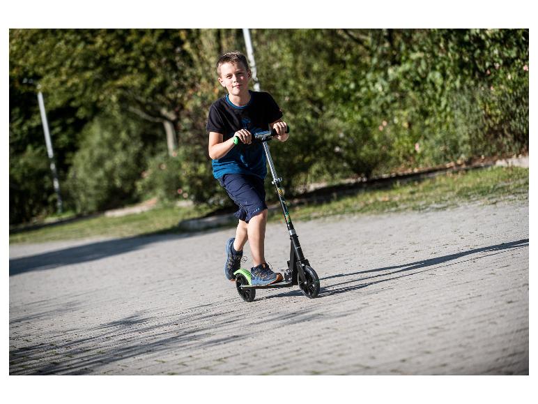 Lächelnder Junge auf einem Roller, in T-Shirt und Shorts, auf einem sonnigen Weg.