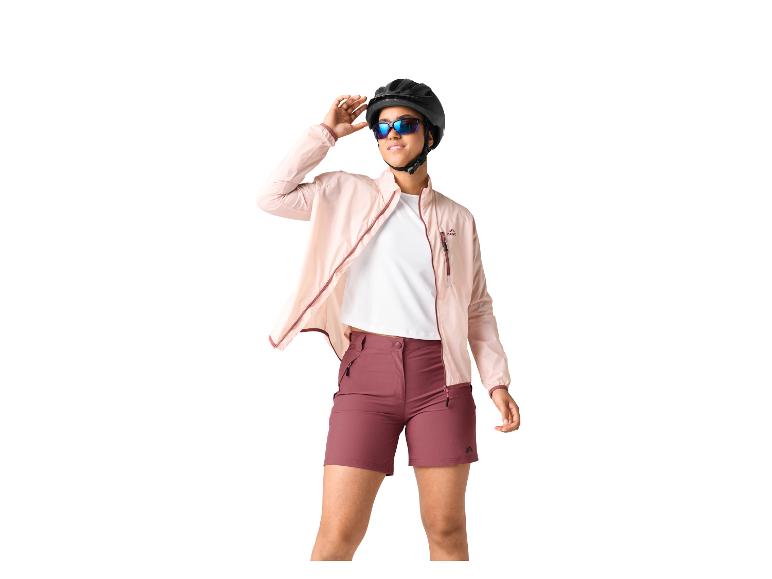 Frau in rosa Jacke, weißem T-Shirt und bordeauxroten Shorts, mit schwarzem Helm und Sonnenbrille.
