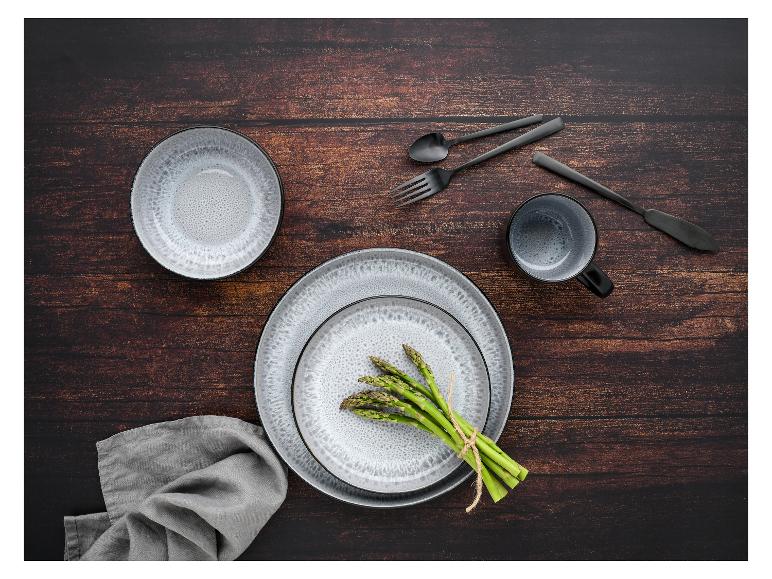 Ein Set grauer, glasierter Teller, eine Tasse und Besteck auf einem Holztisch mit Spargel.