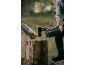 Mann hackt einen Holzstamm mit einer Axt, Holzspäne fliegen in der Luft.