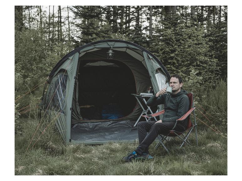 Ein Mann trinkt Kaffee vor einem grünen Zelt im Wald.