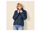 Frau in dunkelblauer Steppjacke und Jeans, mit kurzen blonden Haaren, blickt nach rechts.