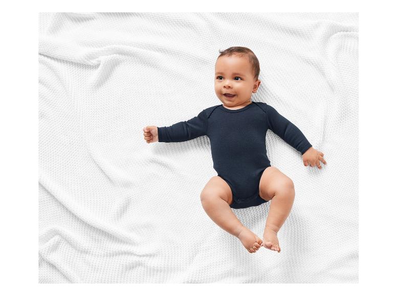 Lächelndes Baby in einem schwarzen Body auf einer weißen Decke.