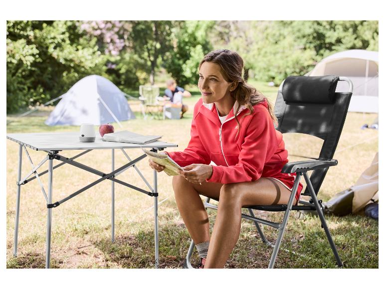 Frau sitzt auf einem Klapp-Campingstuhl und liest eine Karte an einem Campingtisch.