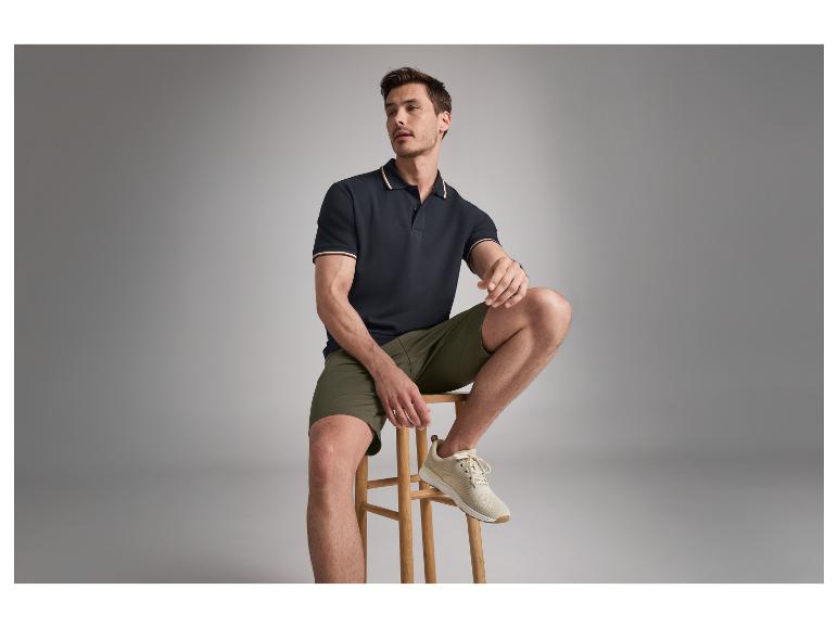 Ein männliches Model trägt ein dunkelblaues Poloshirt und olivgrüne Shorts.